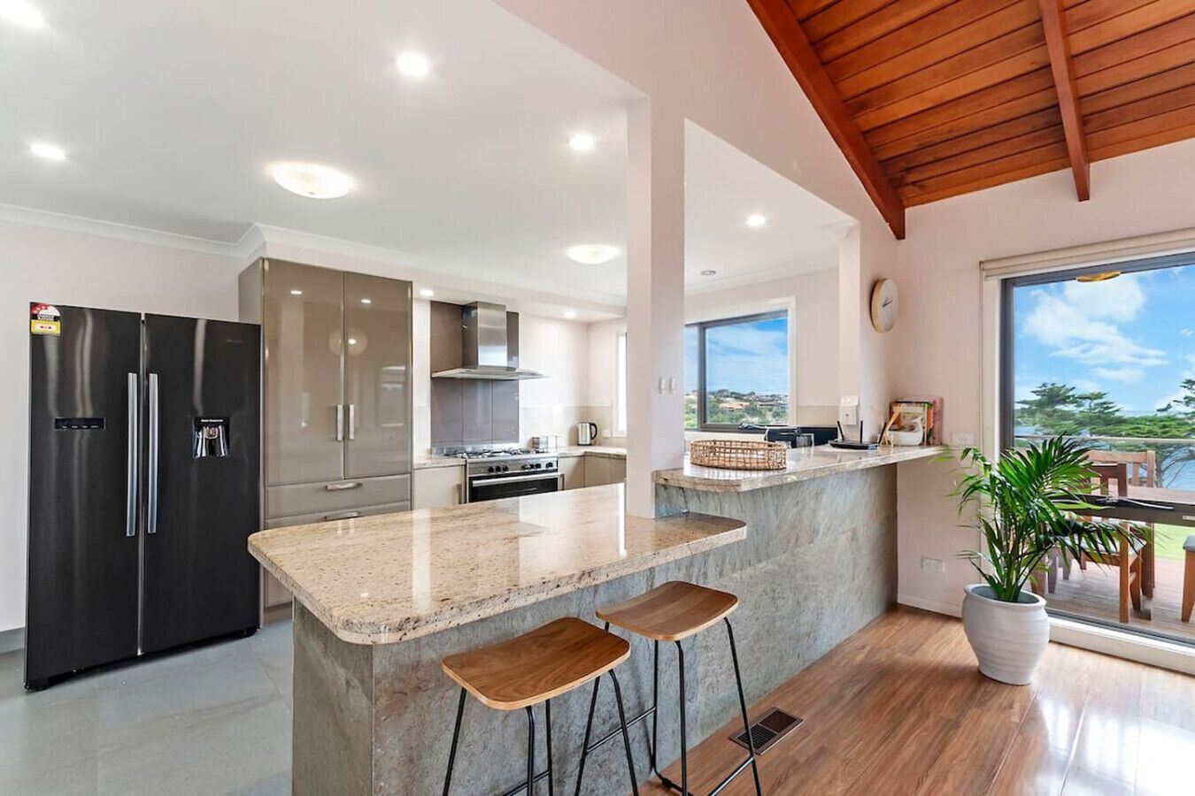 A modern kitchen with a central island, stainless steel appliances, and a view through the window.