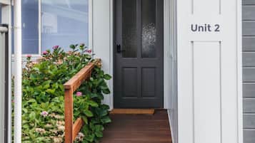 Un edificio con una porta grigia, una scala in legno e un cartello con la scritta 'Unità 2'.