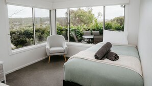 A bedroom with a large window, a bed with rolled towels, a chair, and a view of greenery outside.