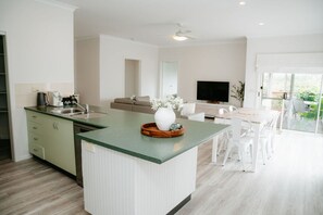 A modern kitchen with a central island, a dining area with white chairs, and a large window providing a view of the outdoors.