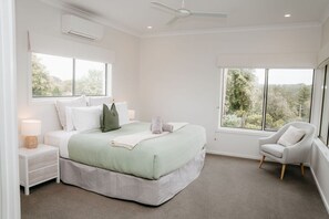 A bedroom with a bed, nightstands, a chair, and large windows.