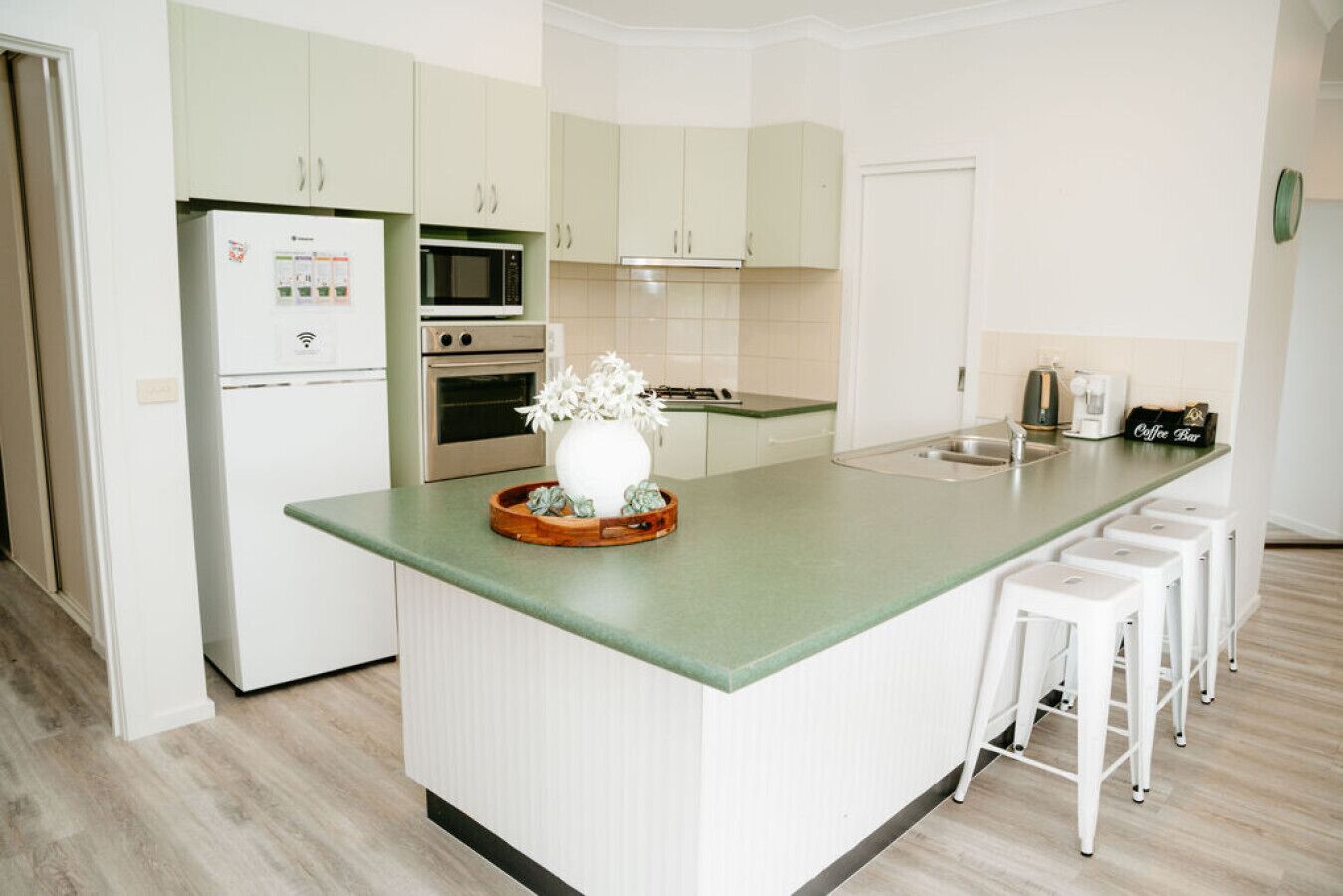 Una cocina moderna con una isla central, armarios blancos, microondas, horno y una estación para café.