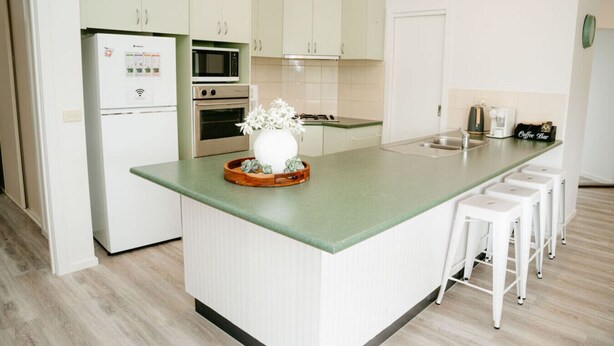 A modern kitchen with a central island, white cabinetry, a microwave, oven, and a coffee station.