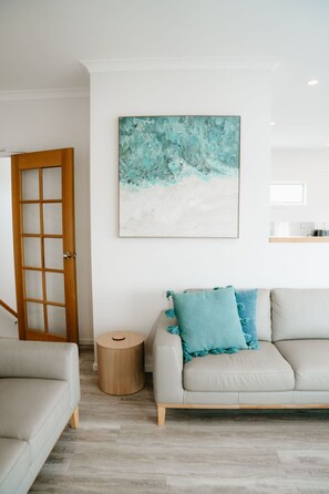 A modern living room with a light-colored sofa, a round side table, and a wooden door. - Port Campbell Coastal Unit 3 (Port Campbell)