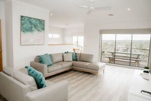 A spacious living room with a large L-shaped sofa, a smaller armchair, and a dining area with a table and chairs. - Port Campbell Coastal Unit 3 (Port Campbell)