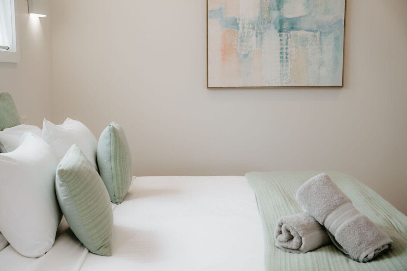 A hotel room with a bed, pillows, a towel, and a painting on the wall.