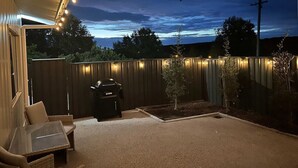 An outdoor patio area with a barbecue grill, seating, and a wooden fence illuminated by string lights.