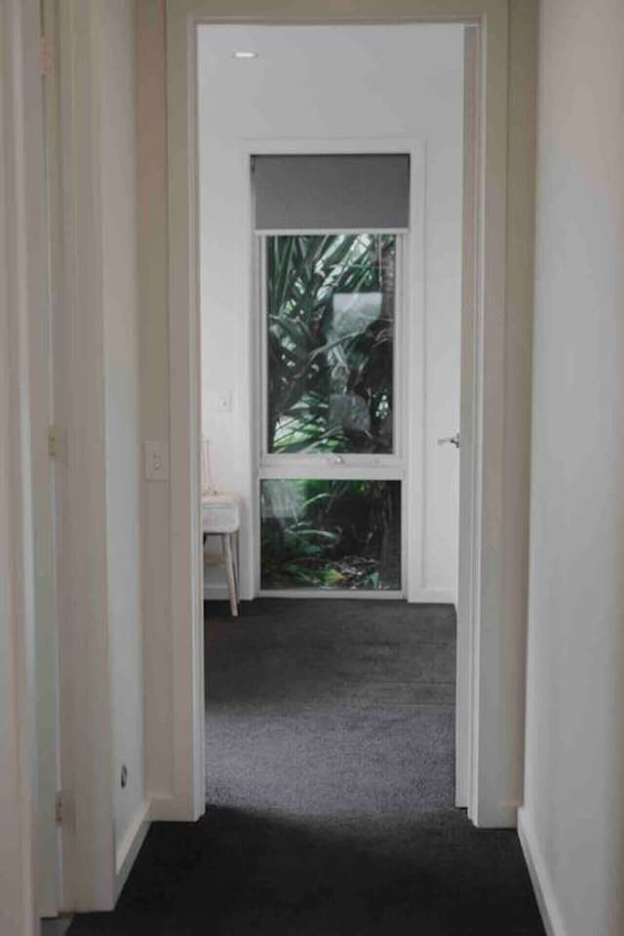 A narrow hallway with a door leading to a room with a large window.