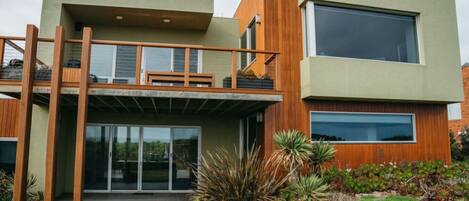 A modern two-story house with a balcony, large windows, and a well-maintained garden.