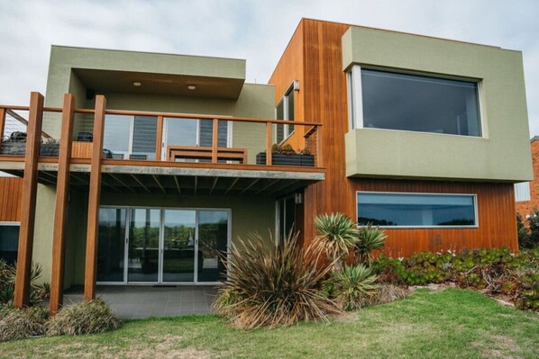 A modern two-story house with a balcony, large windows, and a well-maintained garden.