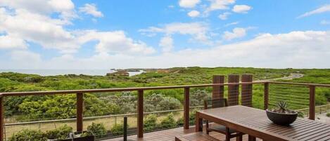 A wooden deck with a table and chairs, overlooking a green landscape with a clear sky.