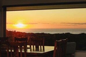 A dining area with a view of the sunset over the sea.