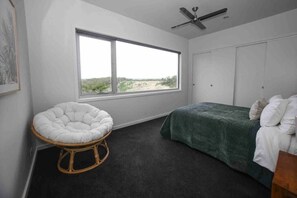 A bedroom with a bed, a chair, a window, and a ceiling fan.