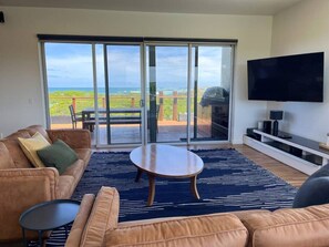 A modern living room with a large sliding glass door leading to a balcony with a view of the ocean.