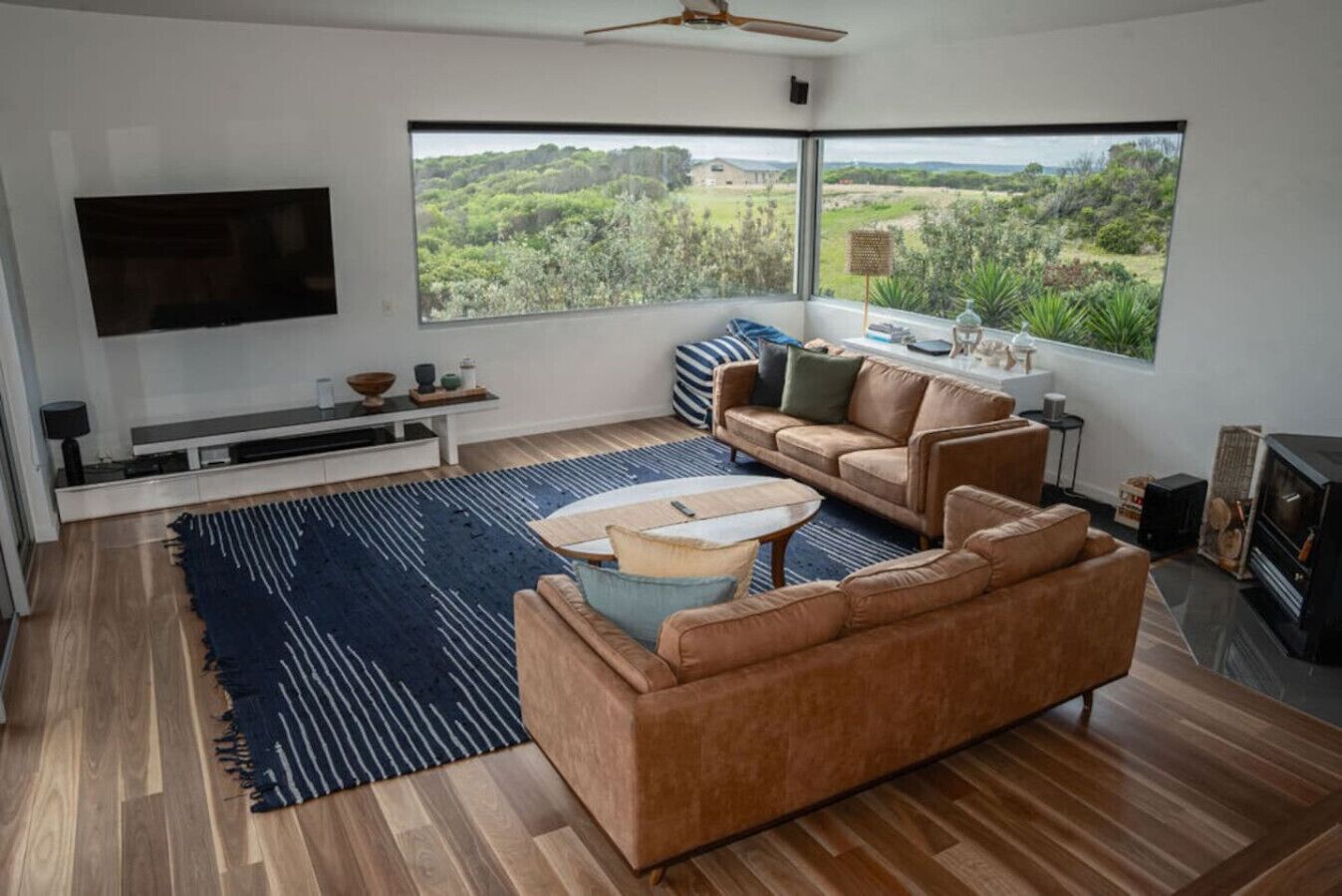 A modern living room with a large window, a flat-screen TV, a sofa, a coffee table, and a fireplace.
