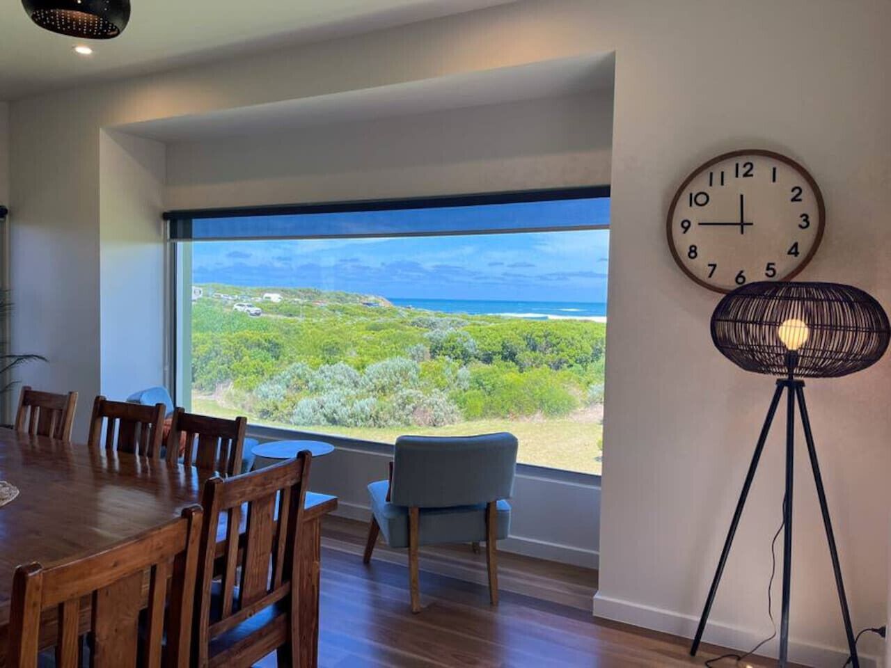 A dining area with a large window, a clock, and a floor lamp.