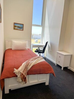 A bedroom with a bed, a chair, a nightstand, and a window.