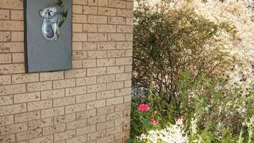 A brick wall with a metal panel featuring a koala and eucalyptus leaves. There are potted plants with green foliage and a pink flower.