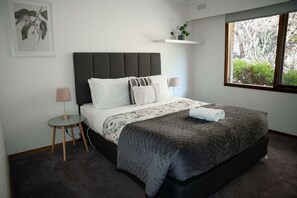 Une chambre à coucher comprenant un lit, des tables de chevet, une fenêtre avec vue et une étagère fixée au mur.