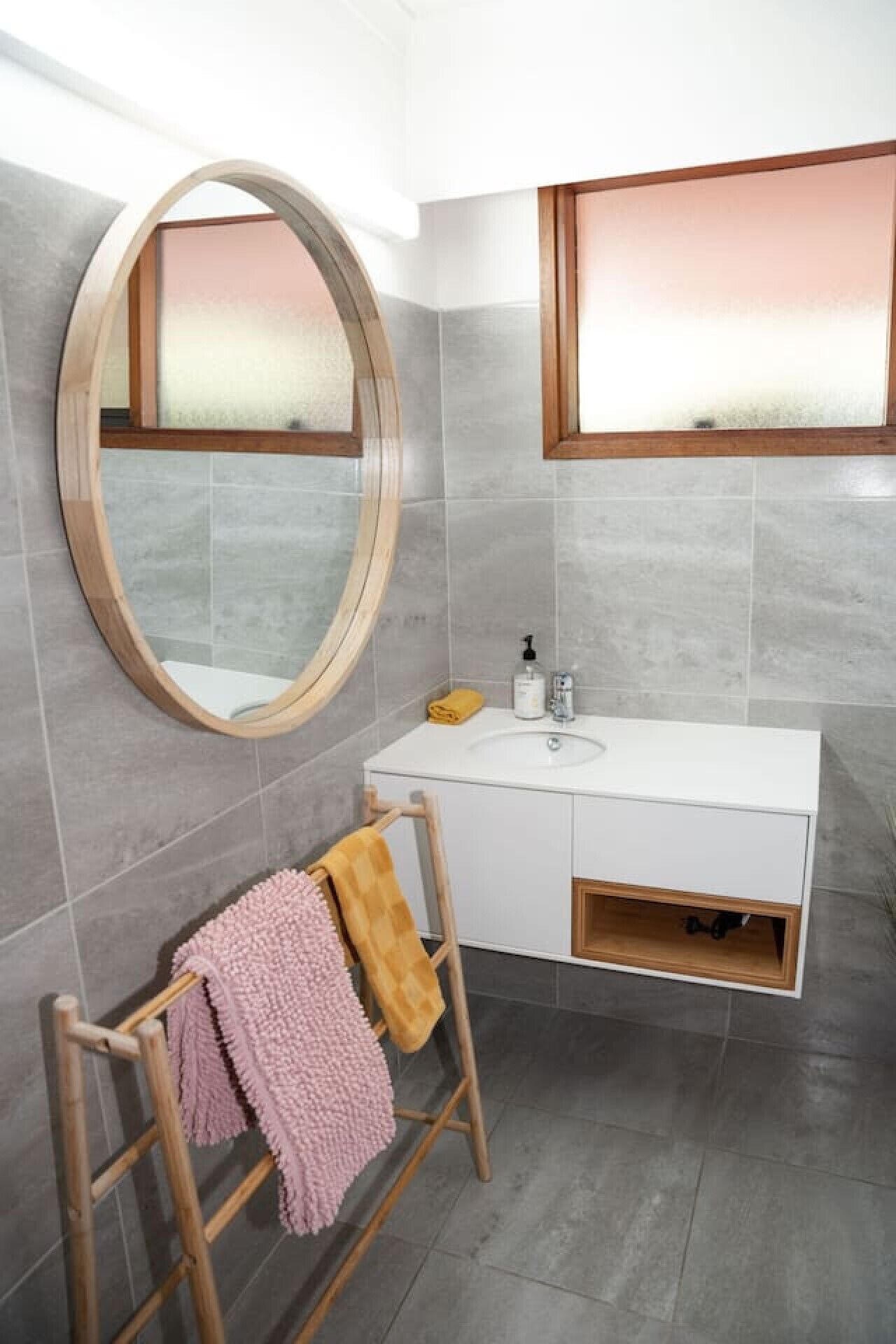 A bathroom with a round mirror, white vanity, and grey tiles.