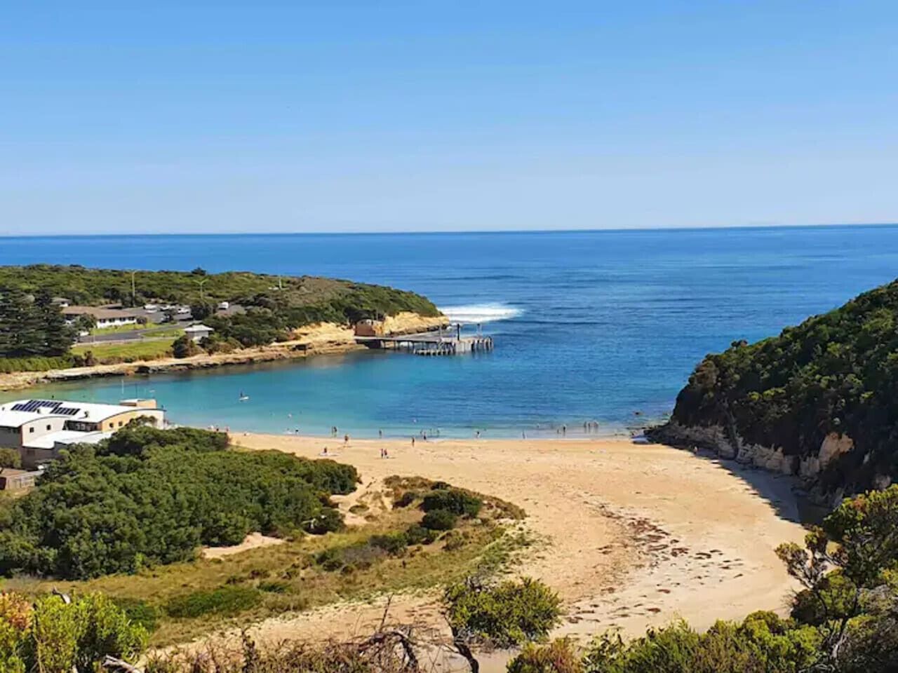 A coastal landscape with a sandy beach, a pier extending into the water, and a building on the left.