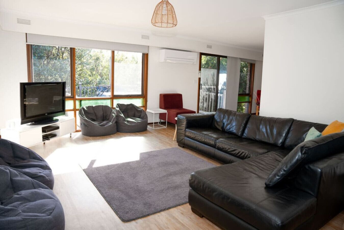 A modern living room with a flat-screen TV, two bean bags, a leather sofa, and a red chair.