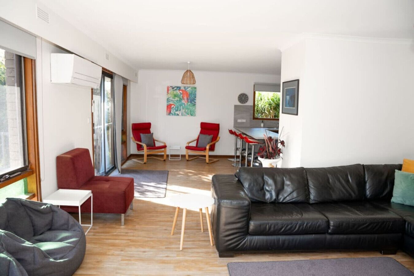 A modern living room with a black leather sofa, red chairs, a small table, and a bean bag.