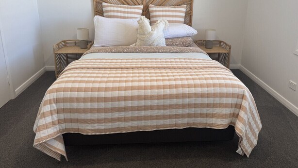 A bed with a checkered bedspread, two pillows, a headboard, and two bedside tables with lamps.