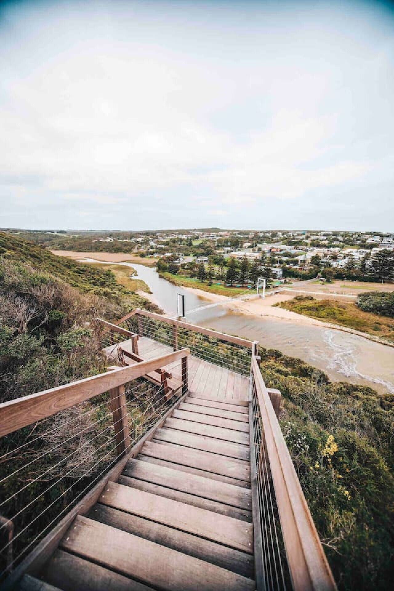 A wooden staircase leading down to a river with a view of a town in the distance.