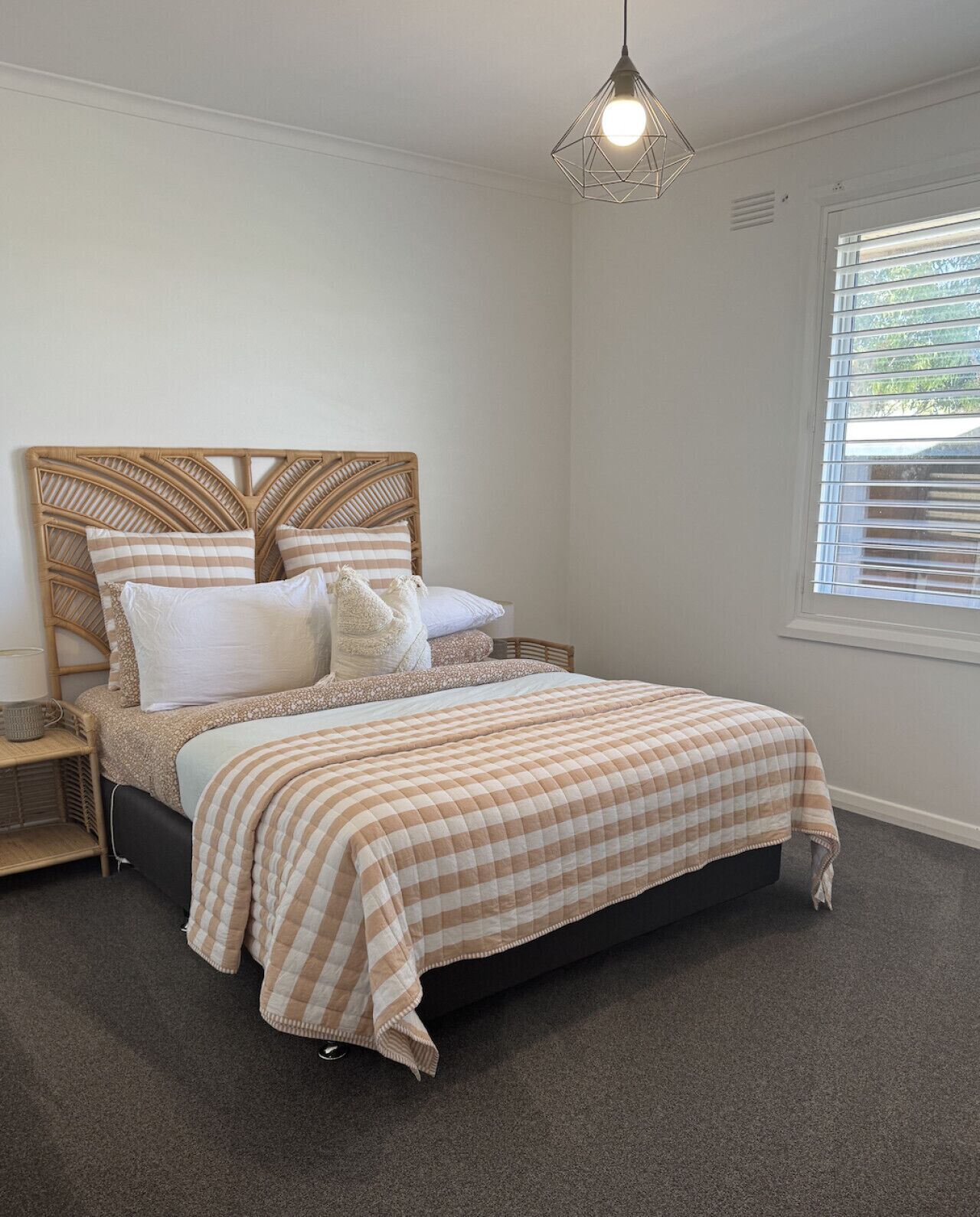 Un dormitorio con cama, mesita de noche, lámpara, ventana con persianas y lámpara colgante.
