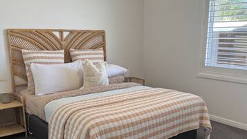 Un dormitorio con cama, mesita de noche, lámpara, ventana con persianas y lámpara colgante.
