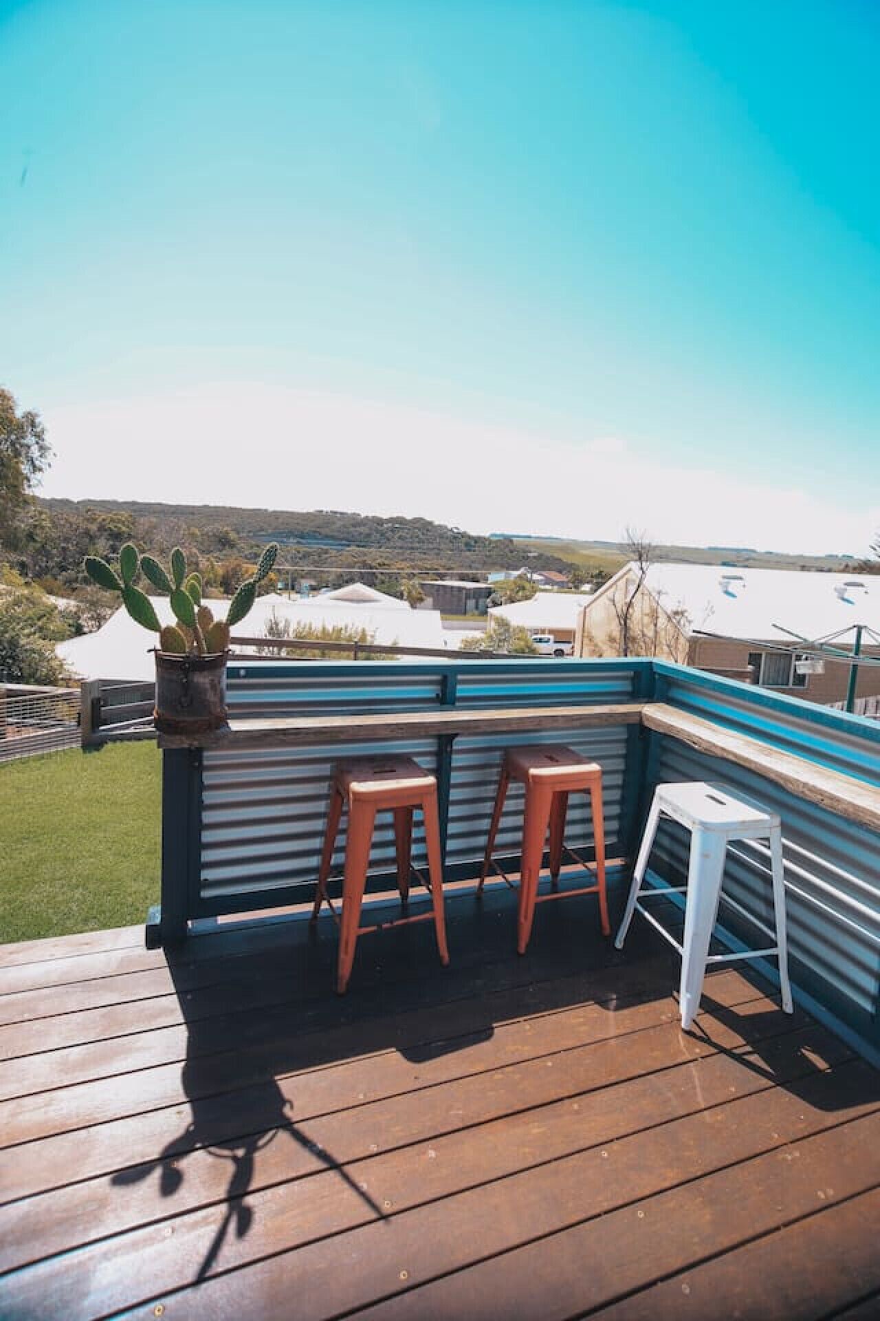 A wooden deck with two stools and a small table, overlooking a landscape with hills and buildings.