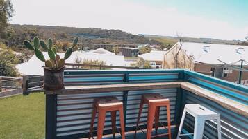 A wooden deck with two stools and a small table, overlooking a landscape with hills and buildings.