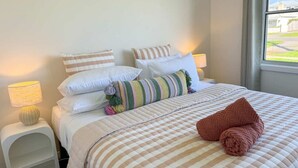 A neatly made bed with a striped bedspread, pillows, and a rolled towel. - Campbell Cottage Port Fairy (Port Fairy)