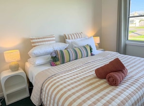 A neatly made bed with a striped bedspread, pillows, and a rolled towel. - Campbell Cottage Port Fairy (Port Fairy)