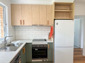 A modern kitchen with wooden cabinets, a built-in oven, a refrigerator, and a window providing natural light. - Campbell Cottage Port Fairy (Port Fairy)