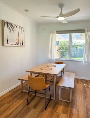 A dining area with a table and chairs, a ceiling fan, a window with curtains, and a painting on the wall. - Campbell Cottage Port Fairy (Port Fairy)
