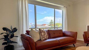A room with a leather sofa, a round wooden table, and a potted plant. - Campbell Cottage Port Fairy (Port Fairy)