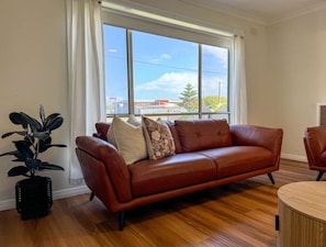 A room with a leather sofa, a round wooden table, and a potted plant. - Campbell Cottage Port Fairy (Port Fairy)