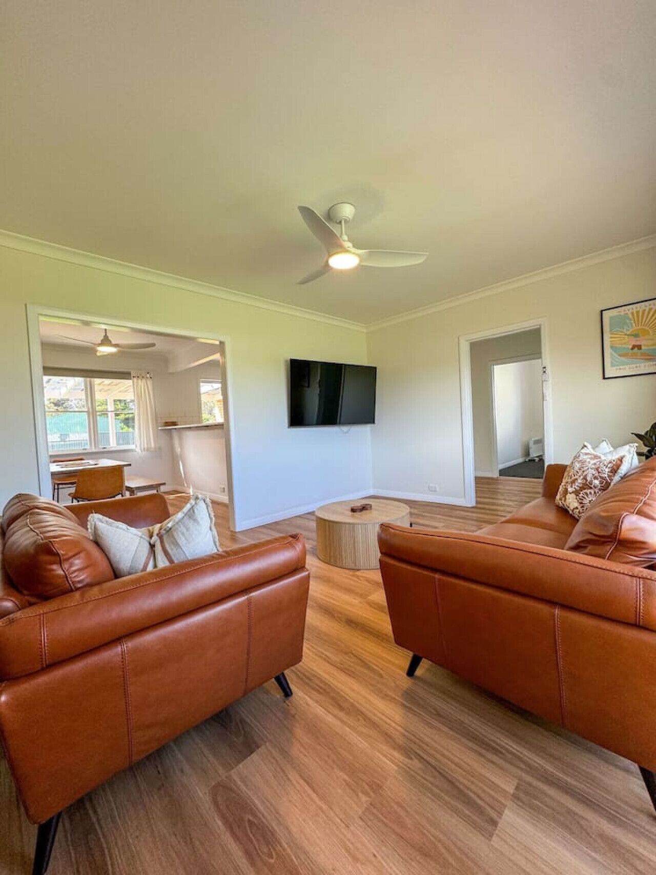 A spacious living area with leather sofas, a flat-screen TV, and a ceiling fan.