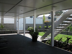A covered outdoor area with a staircase, potted plants, and a view of a building in the background. - Waihi Beach NORTH end and NO roads to cross (Waihi Beach)