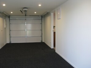 A closed garage door with a ceiling-mounted security camera, a dark carpeted floor, and a plain white wall. - Waihi Beach NORTH end and NO roads to cross (Waihi Beach)