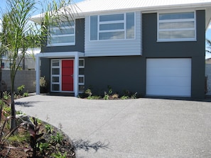 A modern two-story house with a garage, a red door, and a driveway. - Waihi Beach NORTH end and NO roads to cross (Waihi Beach)