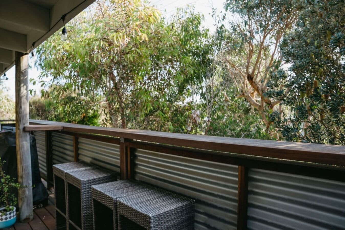 A covered outdoor area with a metal railing, wicker furniture, and a view of dense foliage.