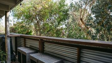 A covered outdoor area with a metal railing, wicker furniture, and a view of dense foliage.
