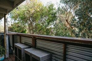 Un espacio exterior techado con barandilla metálica, muebles de mimbre y vista a vegetación densa.
