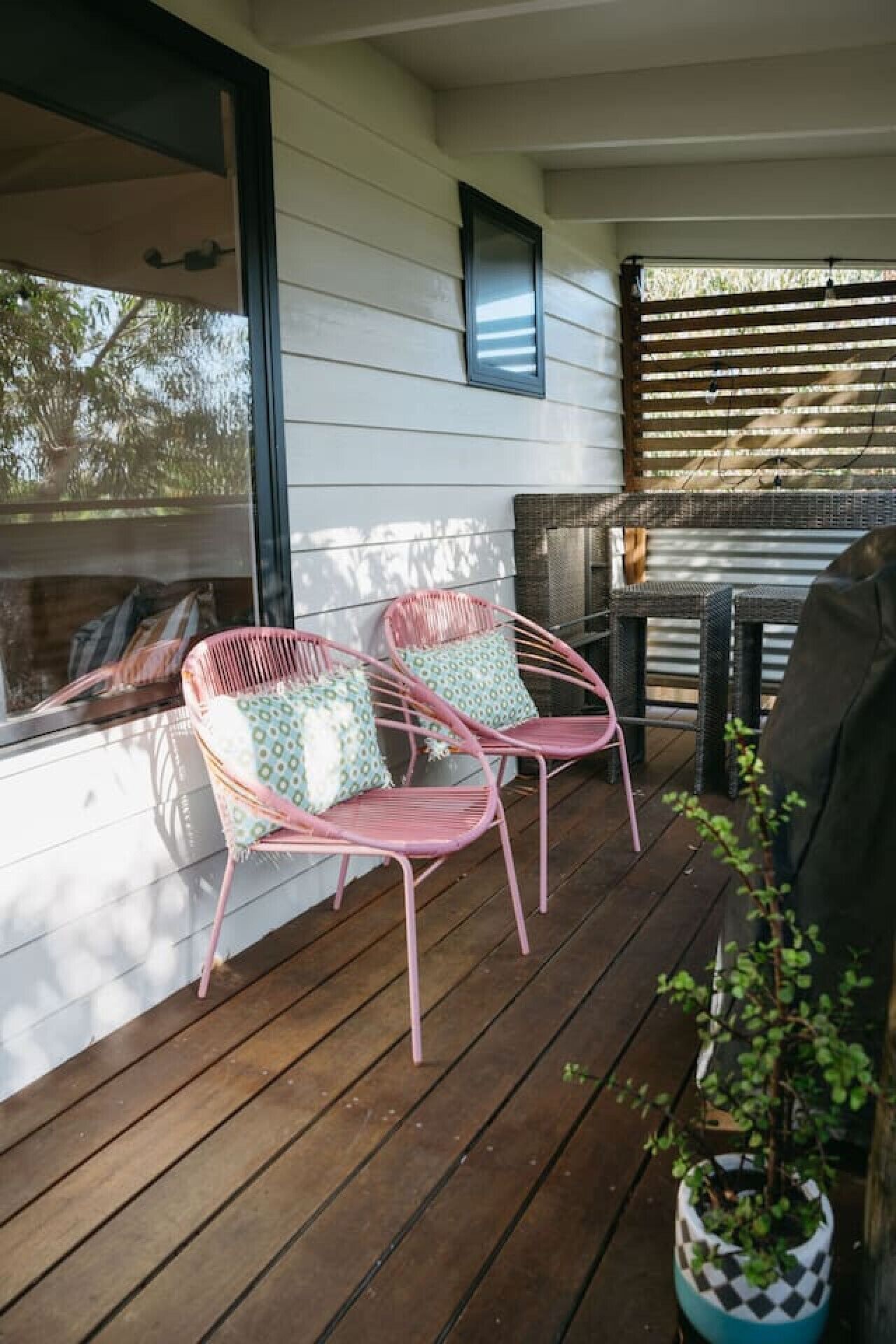 A wooden deck with two pink chairs and a potted plant.