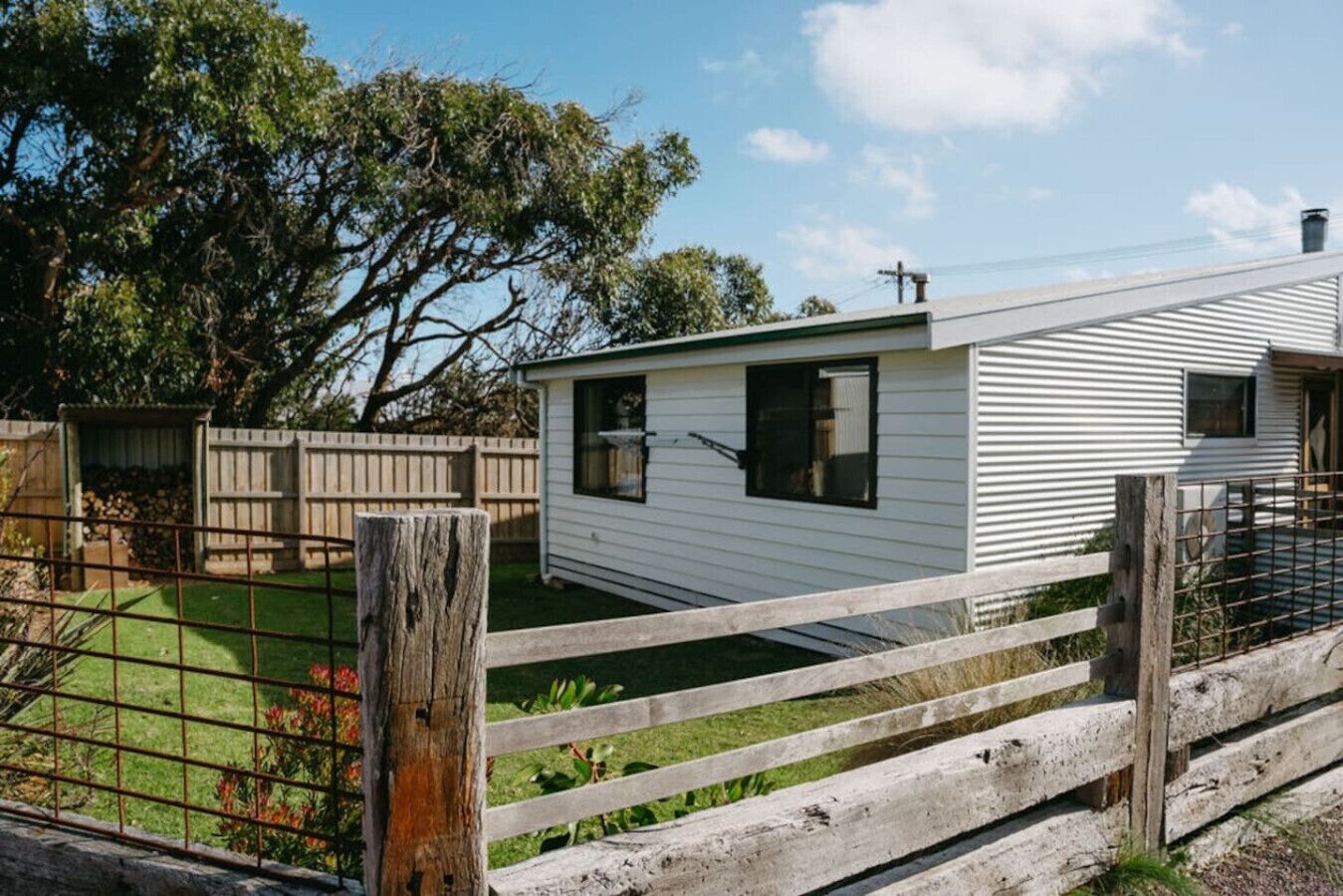 A mobile home with a fenced yard, a small shed, and a tree in the background.