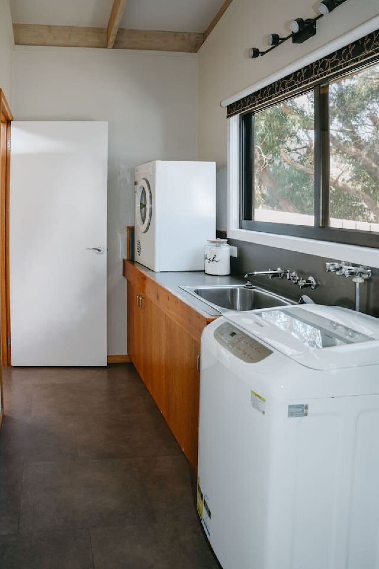 A compact kitchen with a washing machine, a sink, and a window providing natural light.