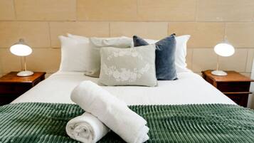 Una cama bien hecha con una colcha verde con textura, almohadas blancas y una toalla blanca enrollada sobre la cama.